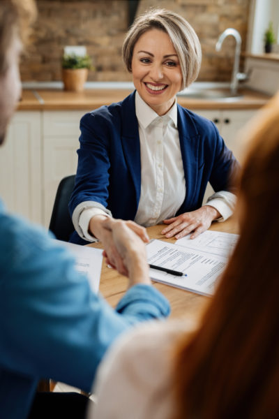 Happy insurance agent shaking hands with unrecognizable couple after the meeting.